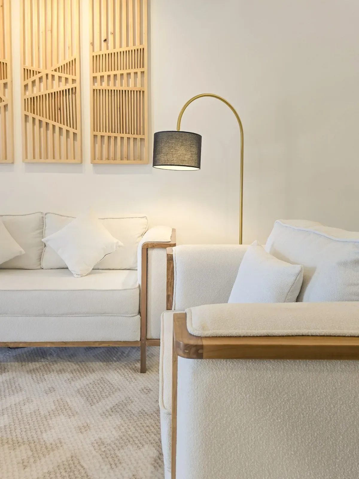 Timber-framed armchair and sofa beneath slatted wall panels, with a black-shaded floor lamp