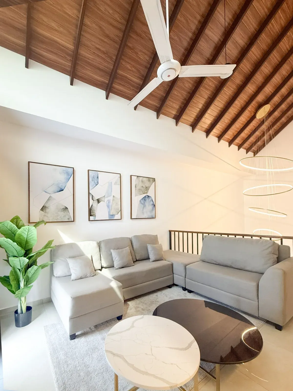 Upper lounge under a timber-clad raked ceiling with a grey sectional sofa and framed art