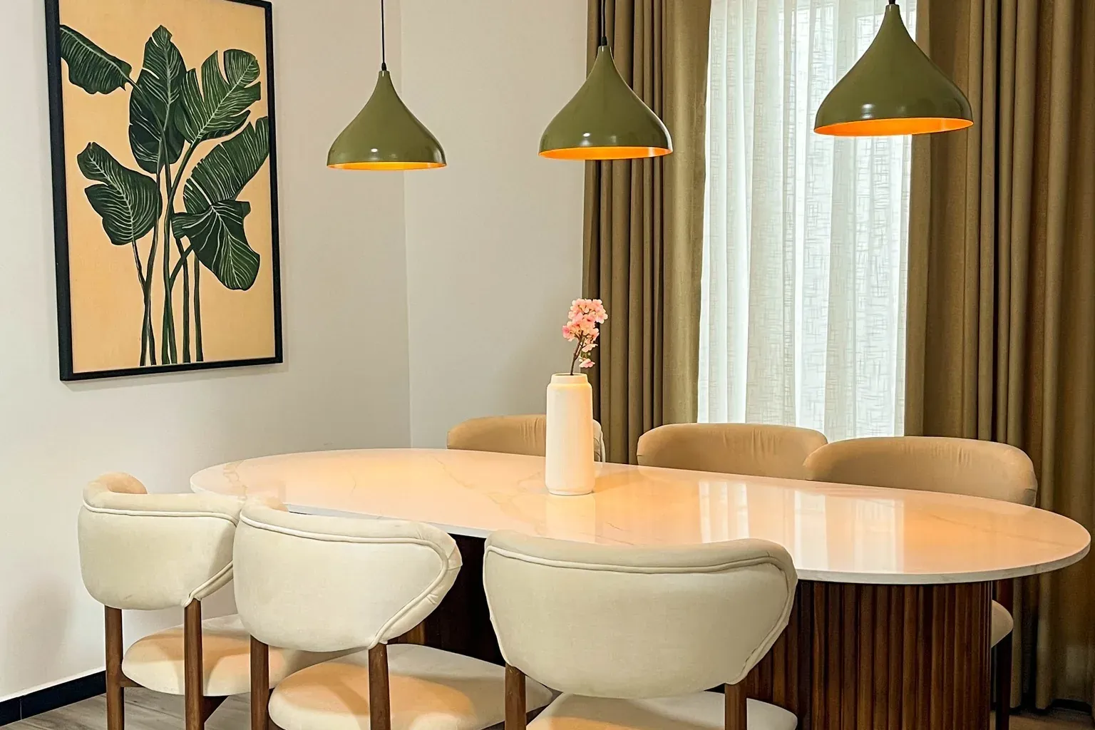 Dining room with an oval pedestal table, curved cream chairs and olive pendant lights