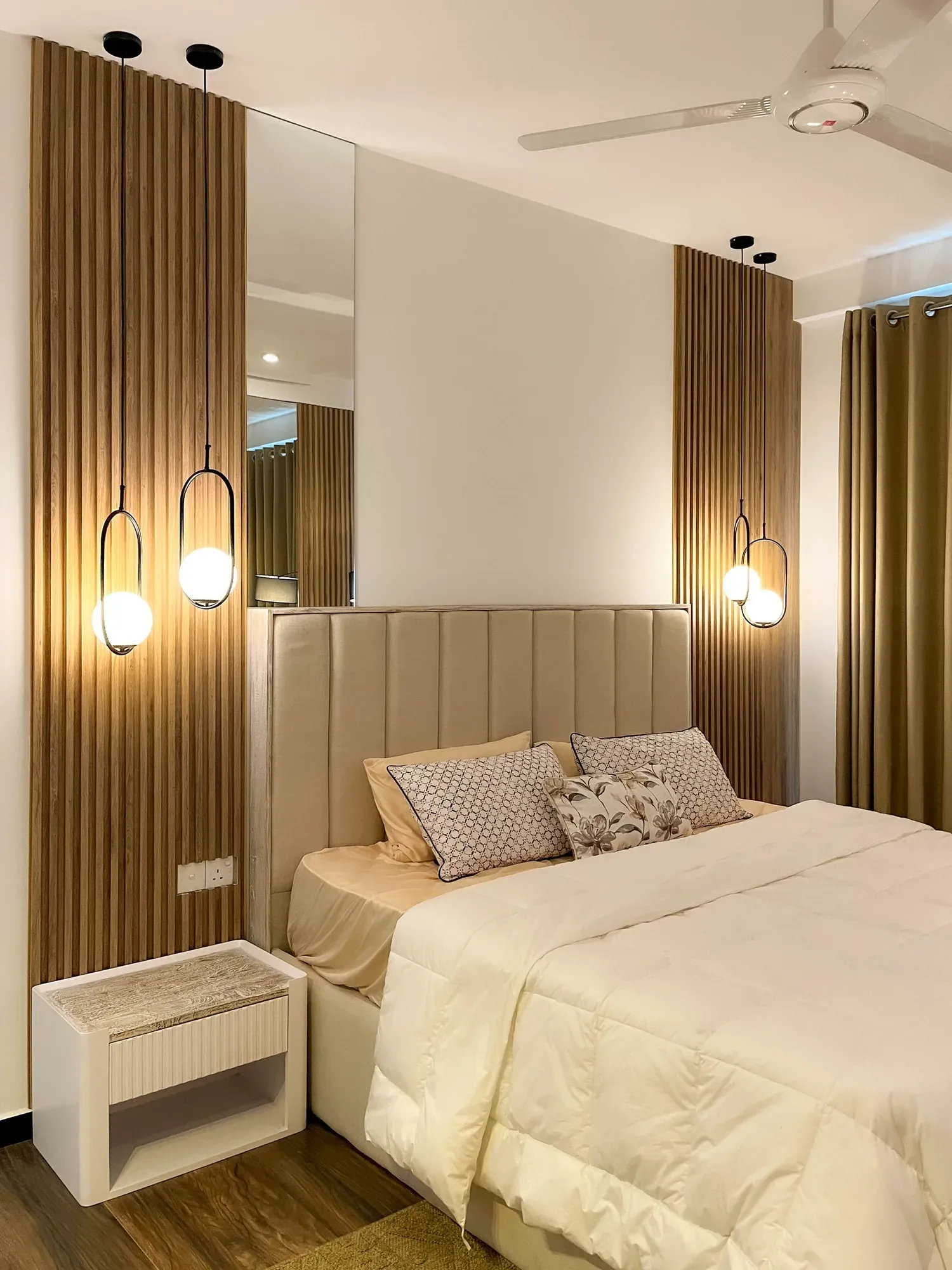 Bedroom with a channel-tufted headboard against a slatted timber wall with pendant lights